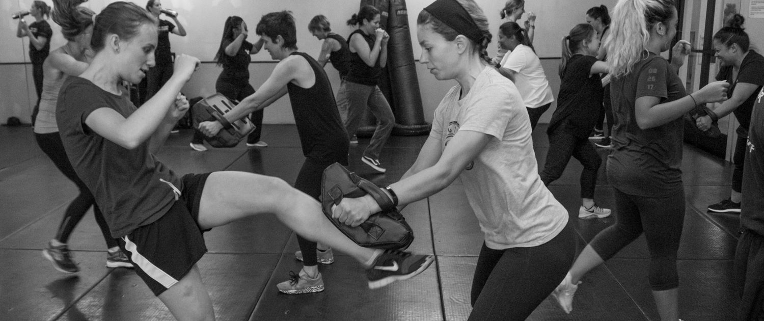 Women training in pairs with kick pads during a self-defense class